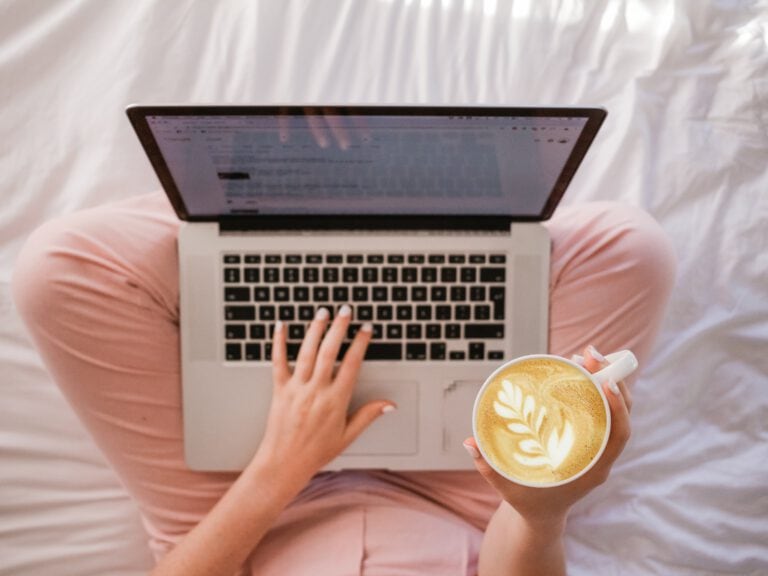 woman using MacBook Pro and holding cappuccino